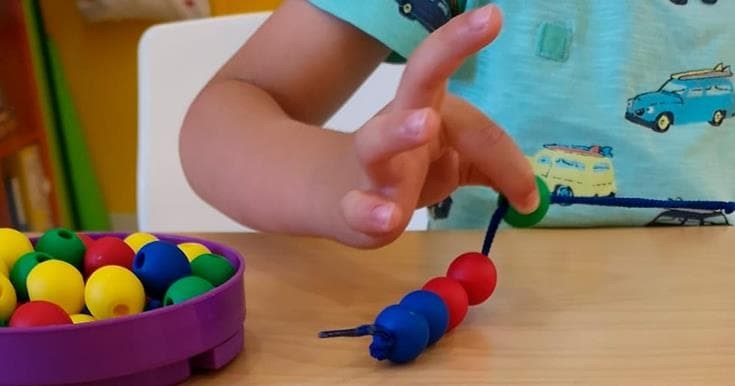 Un niño ensarta bolas de colores en un cordón